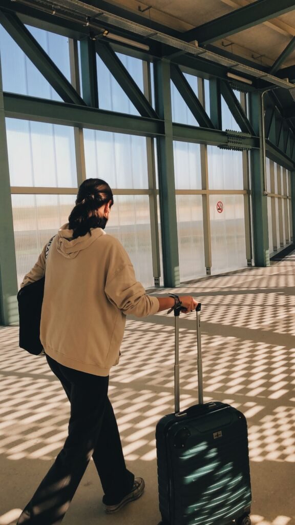 Back view of a woman walking with luggage through an airport terminal.