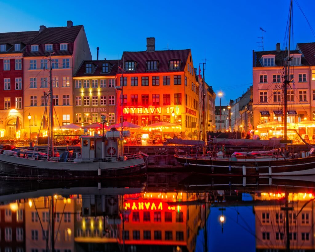 Nyhavn's vibrant waterfront and boats reflected at dusk in Copenhagen, Denmark.