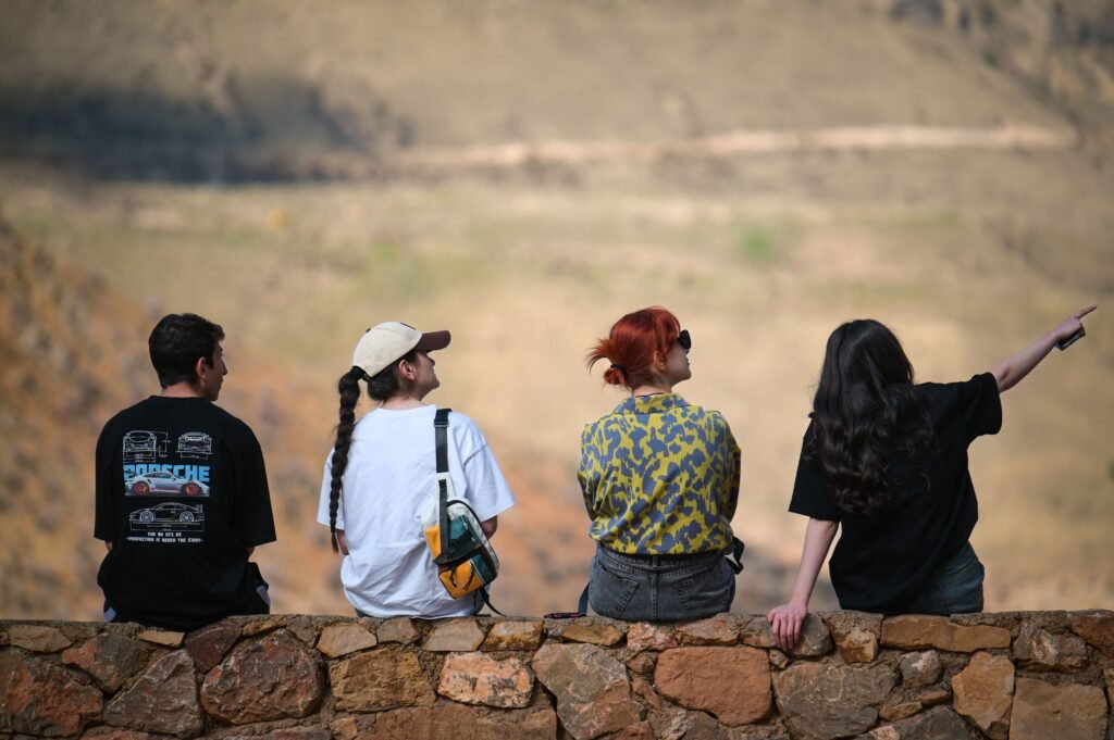 Four friends seated on a stone wall enjoying a scenic mountain view outdoors.