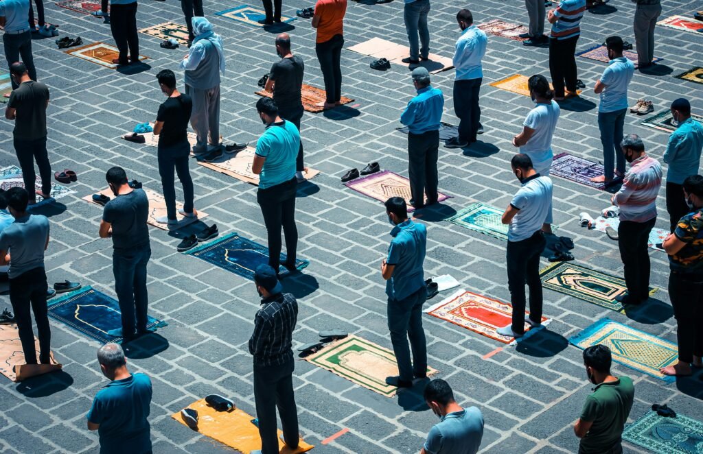Aerial view of a group of men praying on colorful mats outdoors during the day.