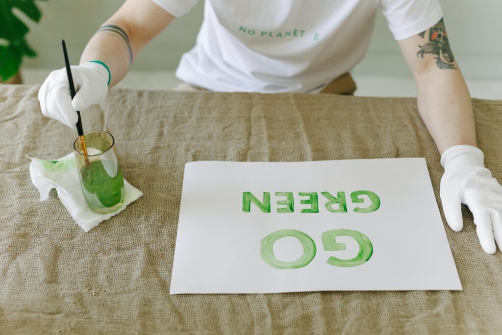 Person painting eco-friendly 'Go Green' message on paper with gloves and brush.